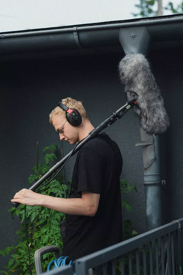 Tontechniker mit Kopfhörern und Boom-Mikrofon bei der Tonaufnahme während eines Outdoor-Filmdrehs für eine Filmproduktion in Salzburg.